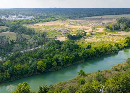 A river flows through a green forest with a town in the distance.