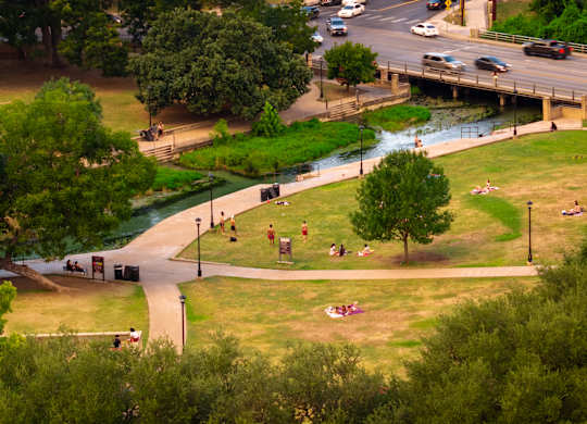 A park with people sitting on the grass and a river running through it.