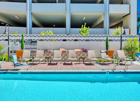 A pool area with a row of chairs and a building in the background.