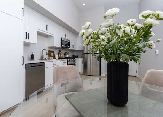 A modern kitchen with a black vase of white flowers on the table.