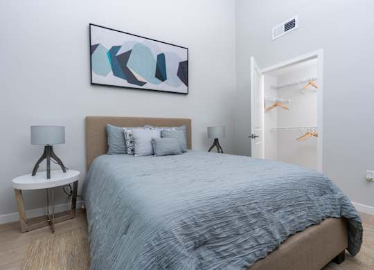 A bedroom with a bed, a side table with a lamp, and a painting on the wall.