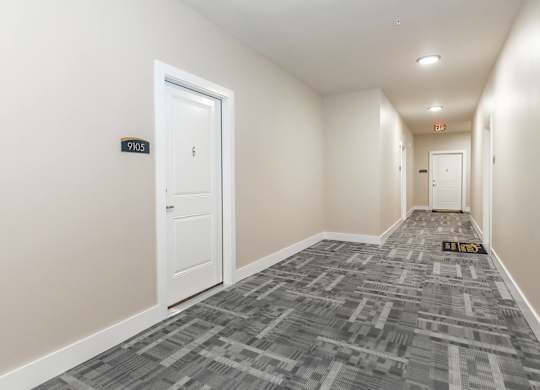 A hallway with a carpeted floor and a door on the left.
