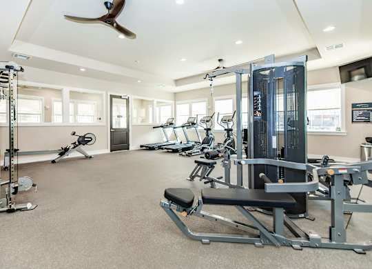 A spacious gym with a variety of equipment including treadmills, weights, and a fan.