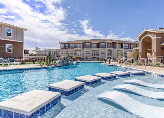 A large swimming pool with lounge chairs in front of apartment buildings.