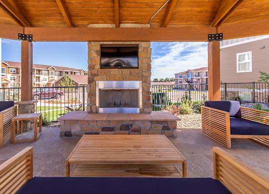 A wooden patio with a stone fireplace and seating area.