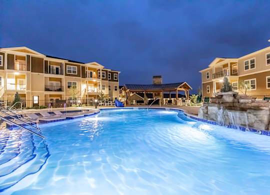 A large swimming pool in front of apartment buildings at night.