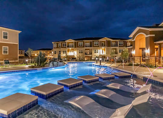 A swimming pool with lounge chairs and apartment buildings in the background.