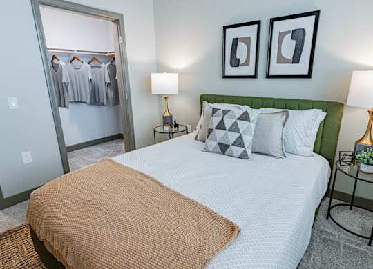 2-Bedroom Luxury Apartments In Burlingame, CA - Bayswater Burlingame - A Modern Bedroom With An Olive Green Tufted Headboard, White Patterned Bedding, And A View Into A Spacious Closet.