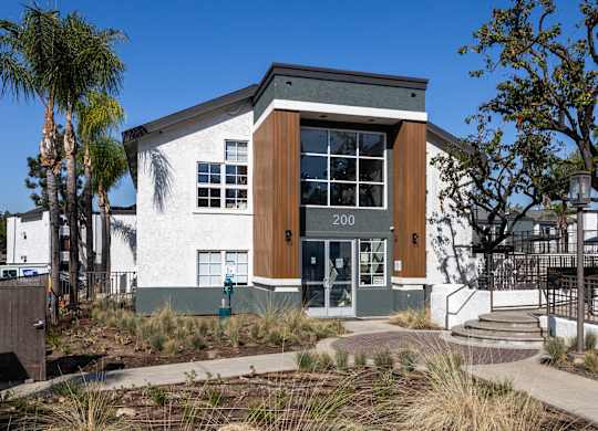 A modern building with a white facade and a brown door is surrounded by palm trees at Verandas Apartments, California