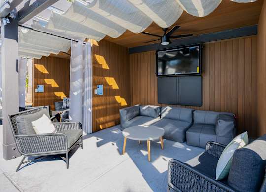 A patio with a grey sofa, a black chair and a white table at Verandas Apartments, West Covina, CA, 91791