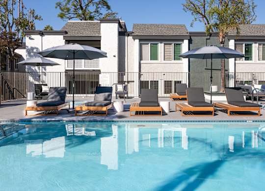A pool with chairs and umbrellas in front of a house at Verandas Apartments, California