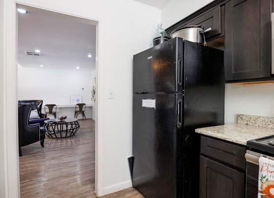 A black refrigerator is in a kitchen with a dining table and chairs in the background.