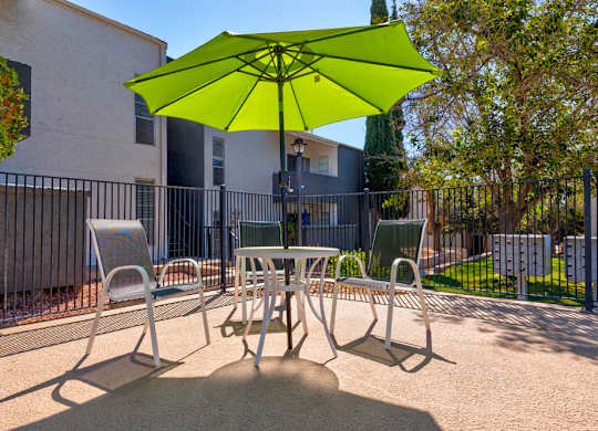 A green umbrella shades a table and chairs in a courtyard.