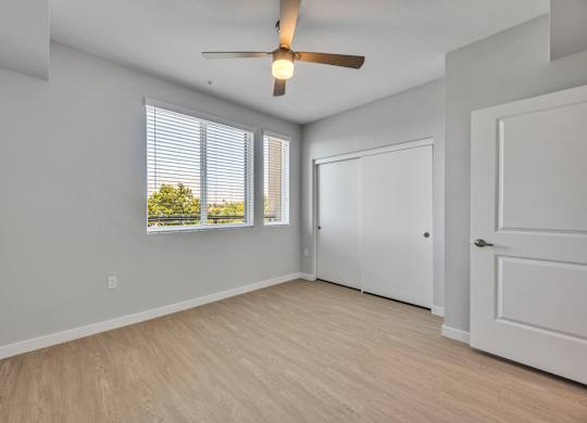 A room with a ceiling fan and a window with blinds.