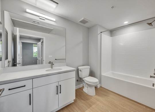 Luxury Apartments Near Downtown Ontario, CA - Downtown Ontario Luxury Apartments - Bathroom with Double Vanity Sink, White Cabinets, Large Mirror, Shower and Bathtub Combo, and Wood Grain Vinyl Flooring.