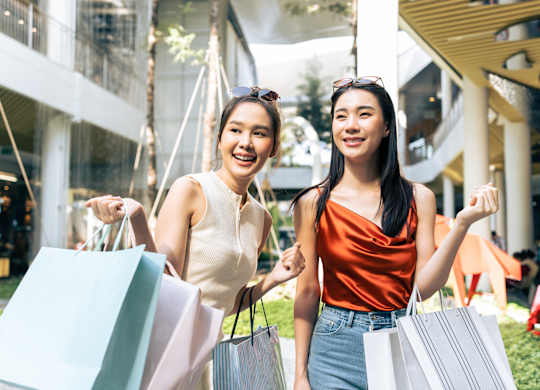 Two women holding shopping bags in front of a building.