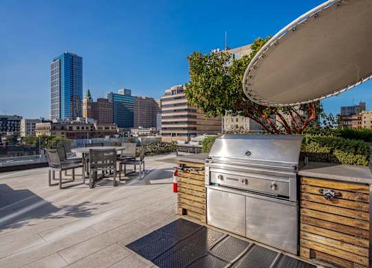 A stainless steel grill is on a patio with a city skyline in the background.