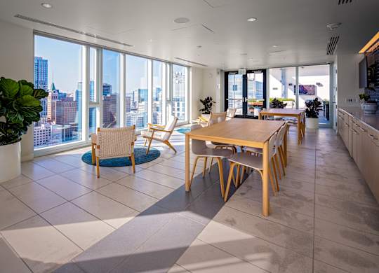 A modern kitchen with a dining table and chairs in front of a large window overlooking a cityscape.