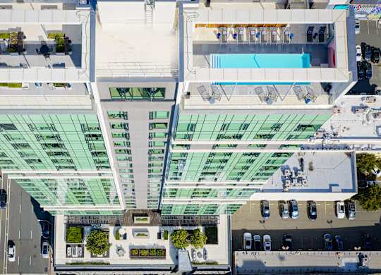 A modern building with a glass facade and a pool on the top floor.
