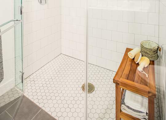 A white tiled shower with a glass door and a wooden stool with towels on it.at The Rise, San Francisco, CA  