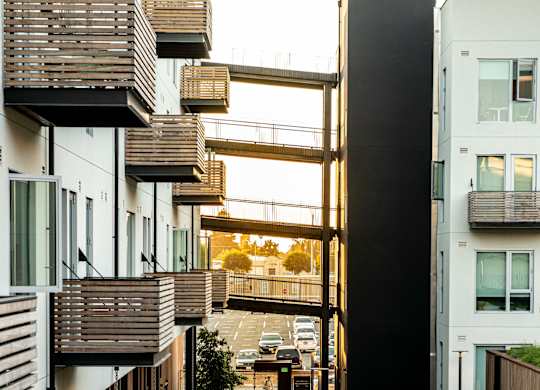 A long, narrow walkway between two buildings with a metal railing on the left and a wooden railing on the right.