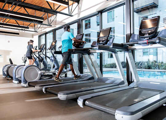 A gym with people exercising on treadmills and elliptical machines.