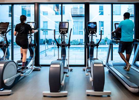 A man and a woman are exercising on treadmills in a gym.