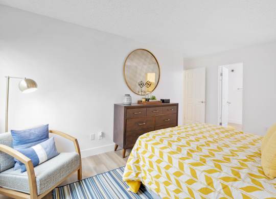 A bedroom with a bed, chair, and dresser at Verandas Apartments, West Covina, California