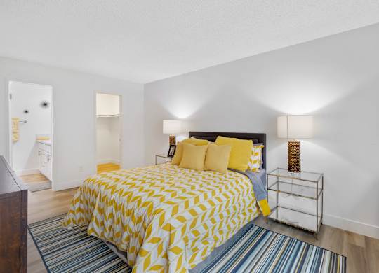 A bedroom with a bed covered in yellow and white bedding at Verandas Apartments, West Covina, California