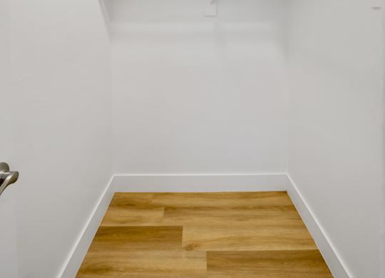 A white hallway with a wooden floor and a door on the left at Verandas Apartments, California