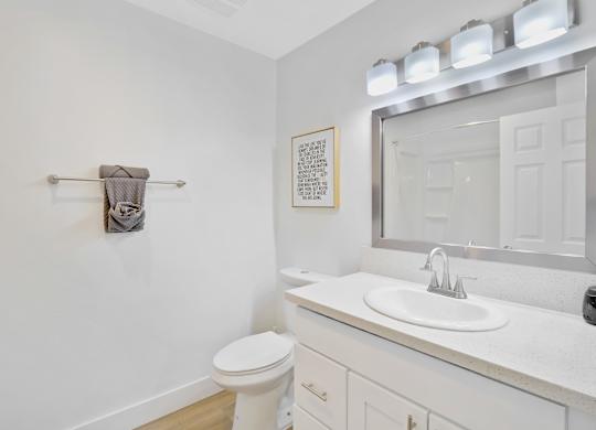 A white bathroom with a toilet, sink, mirror, and a towel rack at Verandas Apartments, West Covina, 91791