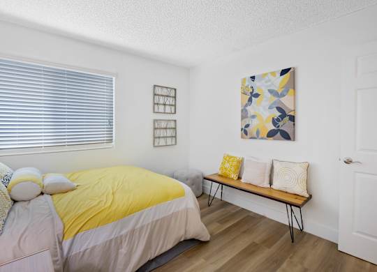 A bedroom with a bed, bench, and artwork at Verandas Apartments, West Covina, California