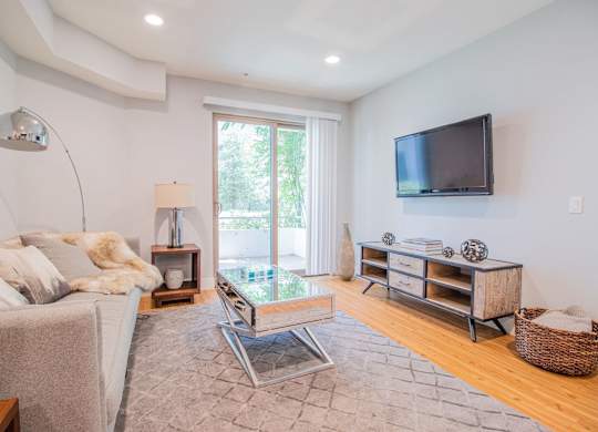 A modern living room with a grey sofa, a glass coffee table, a wooden cabinet, and a flat-screen TV mounted on the wall at Woodley Sara Apartment, Van Nuys, CA