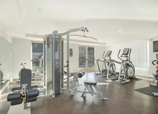 A well-equipped gym with a variety of machines and a person working out on a stationary bike at Woodley Sara Apartment, California