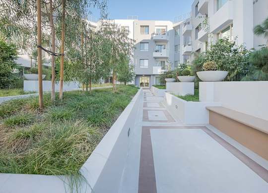 A modern building with a white exterior and a long white pathway leading to the entrance at Woodley Sara Apartment, Van Nuys, California