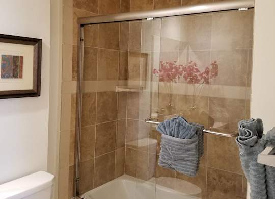 A bathroom with a toilet, a shower with a glass door, and towels hanging on a rack at Woodley Sara Apartment, Van Nuys, CA, 91406