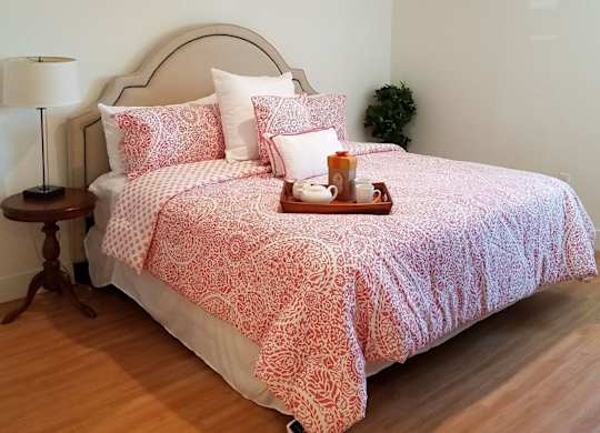 A bed with a red and white patterned comforter and matching pillow cases sits in a room with wooden flooring and white walls at Woodley Sara Apartment, Van Nuys, CA