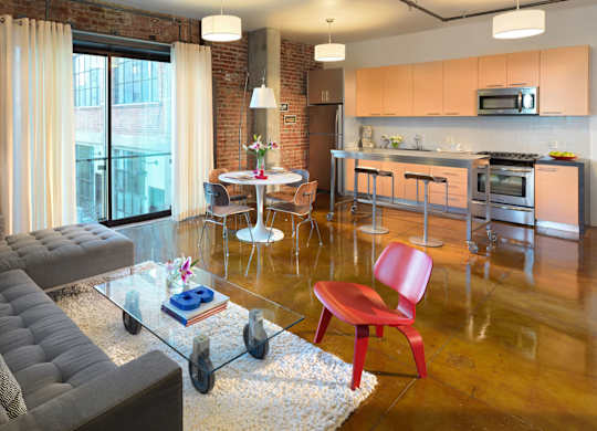 A modern living room with a grey sofa, a red chair, and a glass table.