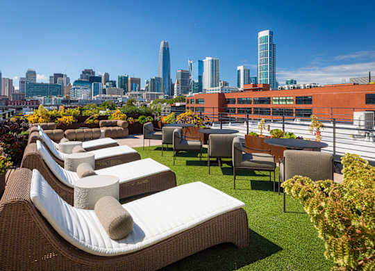 A rooftop patio with wicker chairs and cushions overlooking a city skyline.