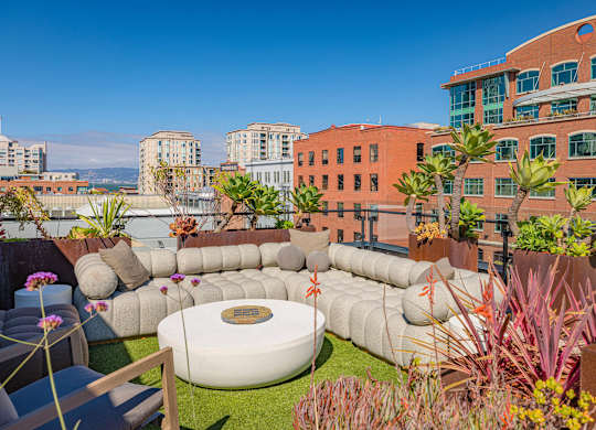 A modern outdoor seating area with a large white circular table surrounded by cushions and plants.