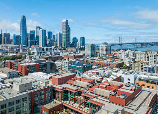 A cityscape with a mix of modern and older buildings, a bridge in the distance, and a clear sky.
