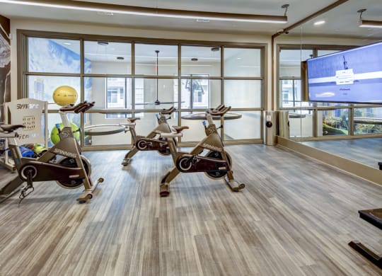 a gym with exercise bikes and a tv on the wall at Arise Riverside, Austin, TX