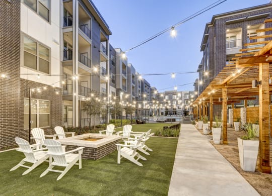Luxury Apartments For Rent In Austin - Arise Riverside - Courtyard With Lush Lawn And Potted Plants, Lounging Area, Firepit, String Lights, And Chairs.