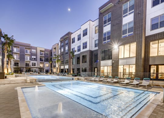 an apartment pool at night with buildings and a moon at Arise Riverside, Austin