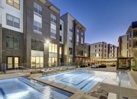 a swimming pool at night with apartments in the background at Arise Riverside, Texas
