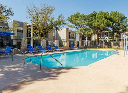 A swimming pool surrounded by trees and a building in the background.