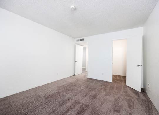 A carpeted room with two doors and a window.