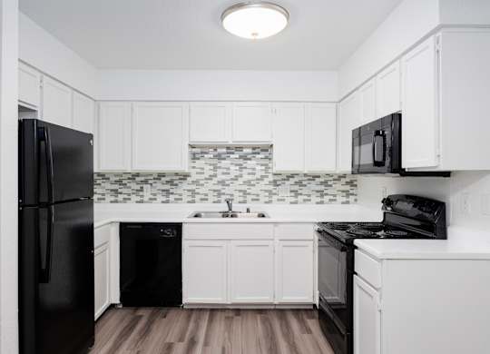 A black refrigerator is in a kitchen with white cabinets.