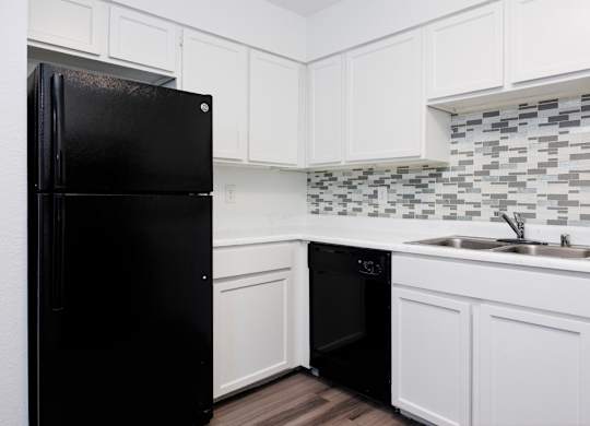 A black refrigerator in a kitchen with white cabinets and a black dishwasher.