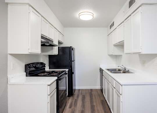 A black refrigerator is in a kitchen with white cabinets.